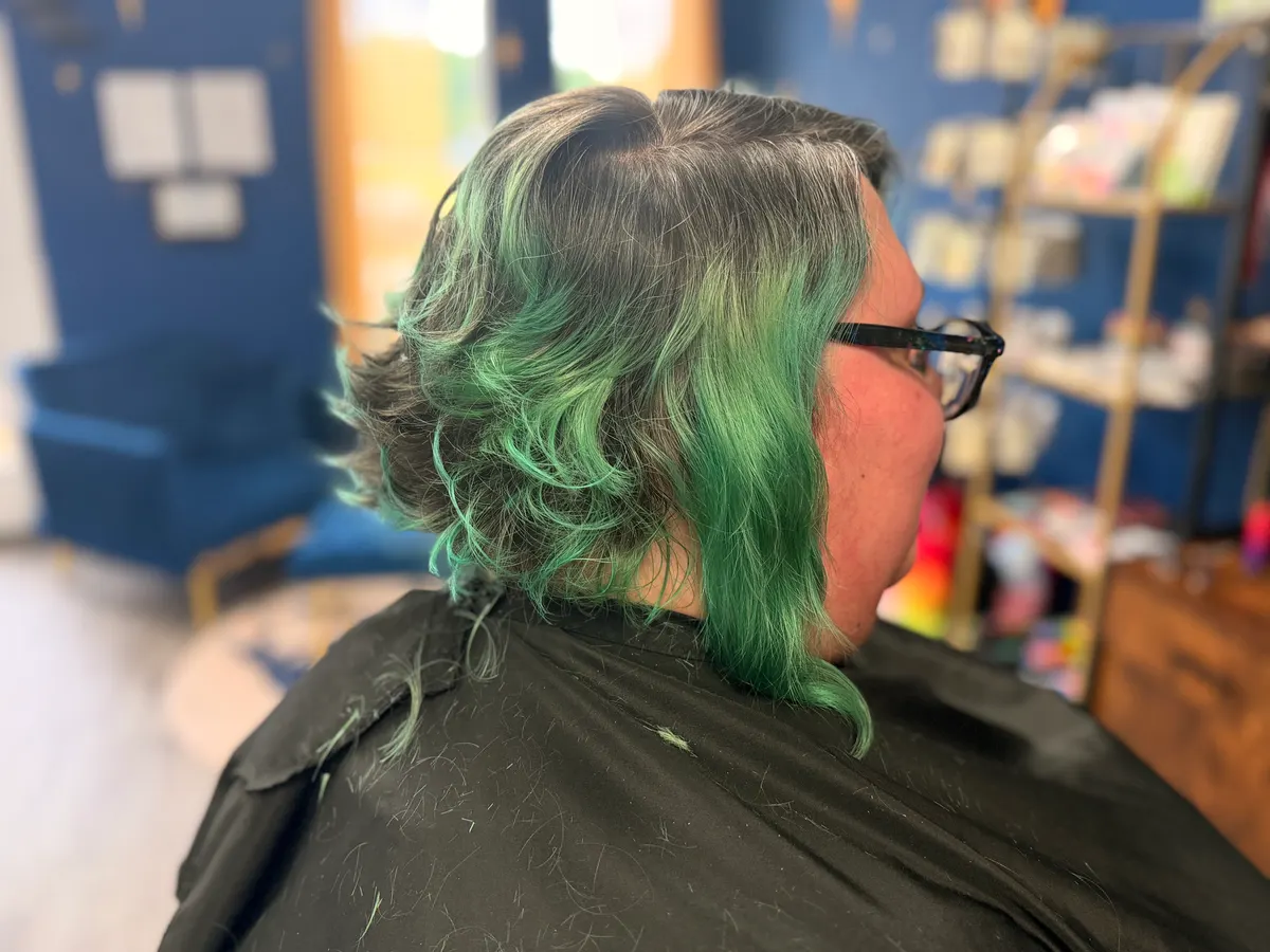 Vivid green ombre curls in soft window light, cut and color by Asher