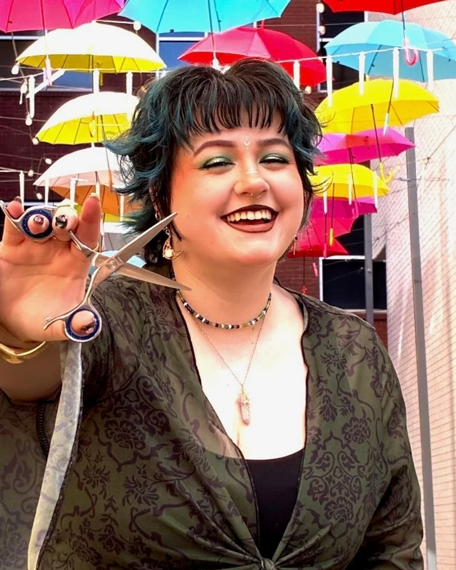 Gray Davenport, vivid color specialist, smiling with teal-green hair while holding styling shears