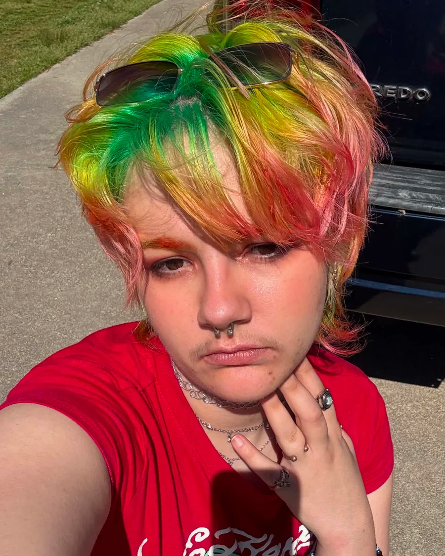 Icarus Tenpenny, hairstylist and colorist, with a green to orange to pink rainbow shag cut and sunglasses pushed up on top
